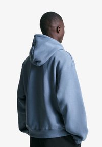 Világoskék kapucnis pulóver, húzózsinórral, bordázott mandzsettával és szegéllyel, laza szabással, puha pamut anyagból készült.