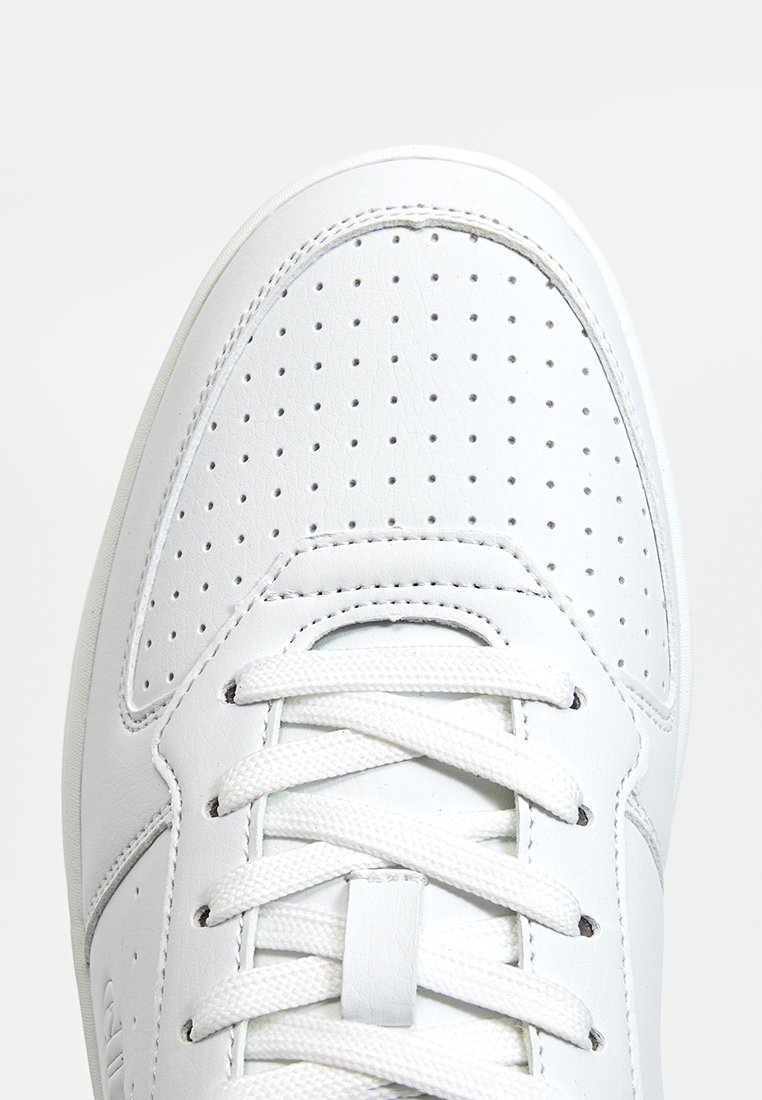 Zapatilla blanca de cuero con caja de dedos perforada, cordones blancos planos y forma redondeada. Textura suave con sutiles detalles de costura.