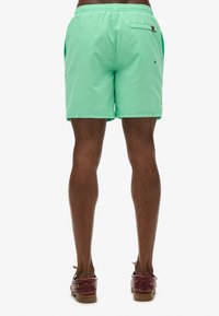 Pantaloni da bagno verde menta con cintura elastica, tasca posteriore e tasche laterali, realizzati in materiale leggero per il comfort.