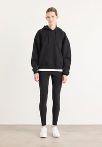Black hoodie with drawstrings, relaxed fit, paired with black leggings and white sneakers. Smooth texture, simple design, no visible patterns.