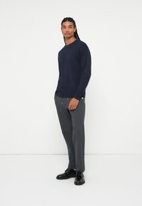 Granatowy sweter dziany zestawiony z szarymi zwężanymi spodniami i czarnymi eleganckimi butami, charakteryzujący się prostym wzornictwem i luźnym krojem.