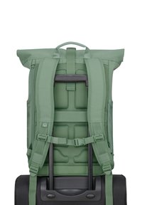 Zöld, felgöngyölhető hátizsák párnázott vállpántokkal, hálós hátrésszel, és rögzítve egy fekete kerekes bőröndhöz. Állítható pántokkal és szerelvényekkel rendelkezik.
