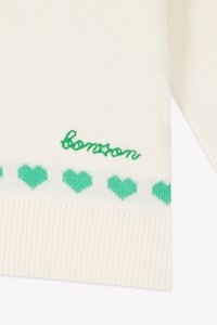 Maglione lavorato a maglia color crema con testo ricamato "bonton" verde e una fila di cuori verdi lungo l'orlo. Texture morbida e leggero.
