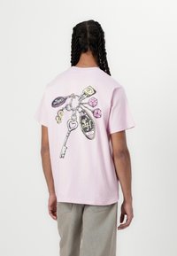 Camiseta de algodón rosa con un gráfico de llaves y dados en la parte de atrás. Mangas cortas, corte relajado y textura suave.