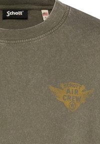 T-shirt Schott Air Crew vert olive avec col rond, petit logo sur la poche avec ailes et emblème étoile, taille L avec étiquette drapeau américain.