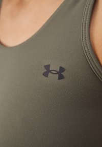 Camiseta deportiva sin mangas de color verde oliva con textura acanalada y logo negro de Under Armour en el pecho. Cuenta con un cuello redondo y diseño sin mangas.