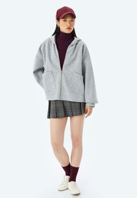 Grå zip-up hættejakke med en frontlomme, parret med en burgundy turtleneck, ternet nederdel, burgundy sokker og hvide sneakers.