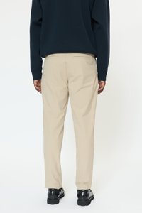 Bež hlače z ravnim krojem, narejene iz gladkega blaga. Imajo zadnje žepe, oblečene z temno modrim puloverjem in črnimi čevlji.