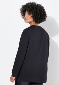 Zwarte longsleeve sweatshirt met een ronde halslijn, ontspannen pasvorm en geribbelde manchetten. Gemaakt van zachte stof met een gladde textuur.