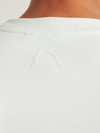 Hanorac gri deschis cu guler cu nervuri, având un mic design triunghiular brodat pe spate, fabricat dintr-un material moale și catifelat.