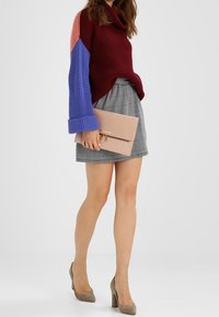 Knit sweater in burgundy, light red, and blue, paired with a grey checkered skirt. Holding a pink clutch. Beige heels complete the look.