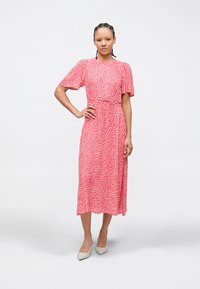 Κόκκινο midi φόρεμα με λευκές πουά, κοντά βολάν μανίκια, ελαστική μέση και φούστα που ρέει. Συνδυάζεται με ανοιχτογκρι μυτερές γόβες.