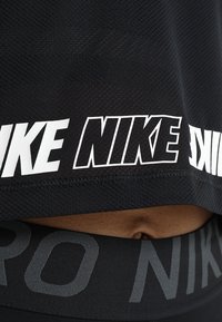 Svart sporttopp med nättextur, med stor vit "NIKE"-logga längs fållen och en åtsittande svart midjeresår under.