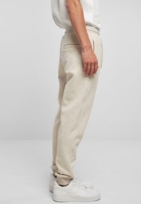 Beige joggingbroeken met een relaxte pasvorm, gemaakt van zacht materiaal, met zijzakken en geribbelde mouwen. Gecombineerd met witte sneakers.