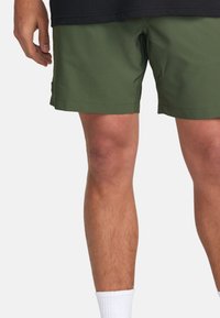 Pantaloni corti verdi in tessuto leggero, con un design semplice, taglio dritto e orlo appena sopra il ginocchio. Sono visibili calzini bianchi.