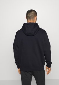 Hoodie noir avec une grande capuche ajustable, texture douce et manches à bords-côtes. L'arrière présente un design sans couture, sans logos visibles.