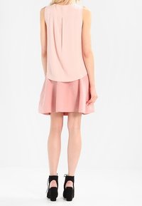 Ljusrosa ärmlös topp med veckad baksida, kombinerad med en matchande rosa utsvängd kjol. Svarta klackstövlar vid ankeln fulländar outfiten.