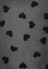 Sorte mønstrede tights med små sorte hjerteformer på en gennemsigtig, tekstureret baggrund med lodrette striber.