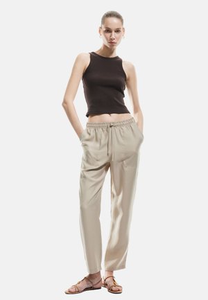 Top corto negro de canalé, pantalones beiges con cintura elástica, tejido ligero, corte relajado, sandalias planas con tiras finas, diseño minimalista, colores neutros.