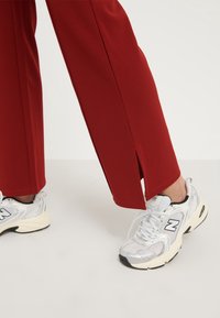 Pantalons rouges ajustés avec des fentes sur les côtés au niveau de l'ourlet, associés à des baskets en mesh blanches avec des accents noirs et une semelle texturée.