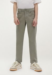 Licht olijfgroene jeans met een rechte pasvorm, vijf-pocket ontwerp en een knoopsluiting, gedragen met beige sneakers met witte veters.