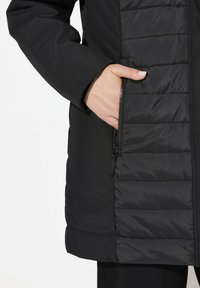 Cappotto nero in tessuto liscio con motivo a quadrati trapuntati sul davanti. Tasca laterale con zip e chiusura nascosta.