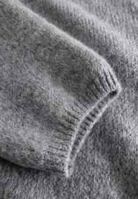 Maglione grigio chiaro realizzato con un morbido filato misto lana a effetto texture. Primo piano del polsino con motivo a coste, che evidenzia la vestibilità aderente.