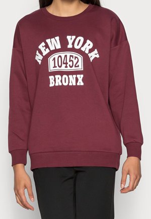 Vinrød sweatshirt med hvid tekst "NEW YORK 10452 BRONX". Den har rund halsudskæring, lange ærmer samt ribbede manchetter og kant.