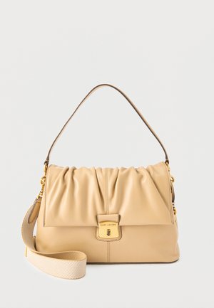Sac bandoulière en cuir beige Marc Jacobs avec rabat froncé, fermoir doré et bandoulière large en tissu détachable sur fond uni.