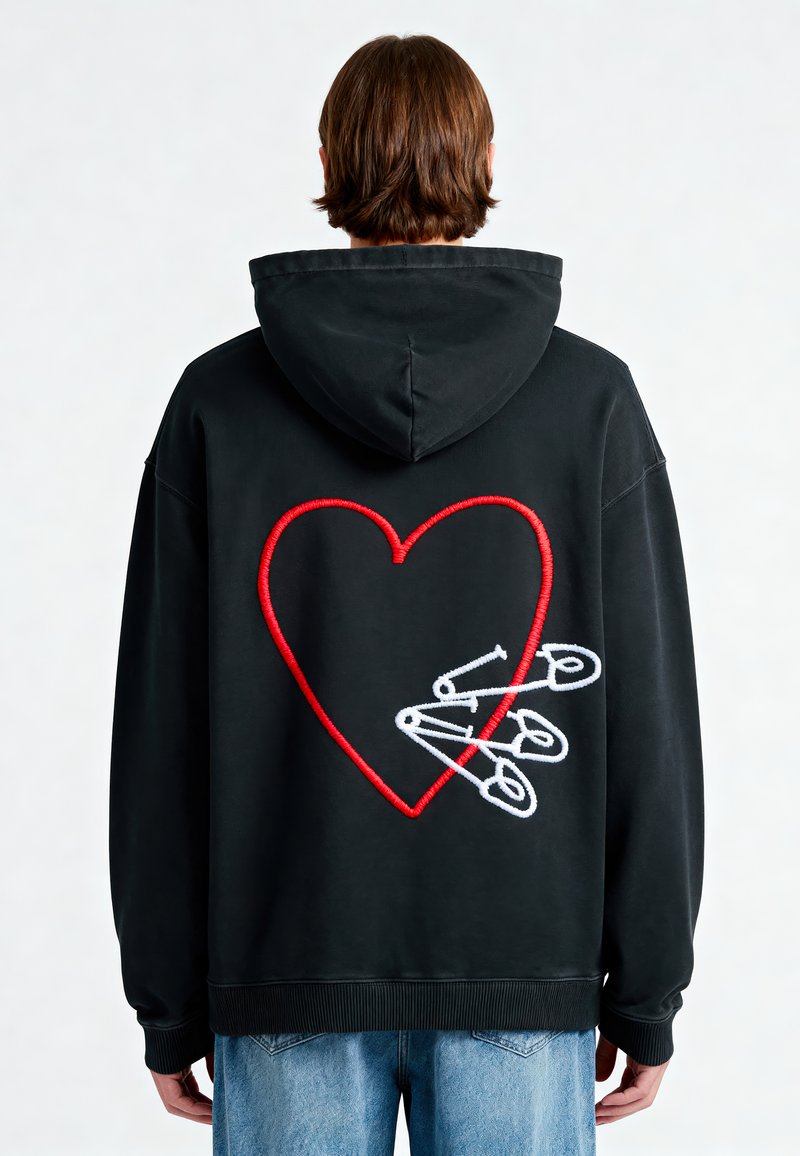 Felpa nera con un grande cuore rosso ricamato sul retro, con spilli di sicurezza bianchi. Vestibilità ampia con cappuccio regolabile e polsini a costine.
