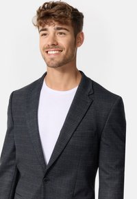 Tailliertes Blazer in Dunkelgrau mit Karomuster, Reverskragen, einreihiger Knopfverschluss und weicher Textur über einem weißen T-Shirt.