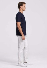 Marineblauwe korte mouwen t-shirt, van katoenmateriaal, met ronde hals, gecombineerd met witte katoenen broeken en witte sneakers, gezien vanaf de zijkant.