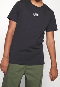 Camiseta negra de algodón con un pequeño logo blanco de "The North Face" en el pecho izquierdo. Mangas cortas con un corte clásico.