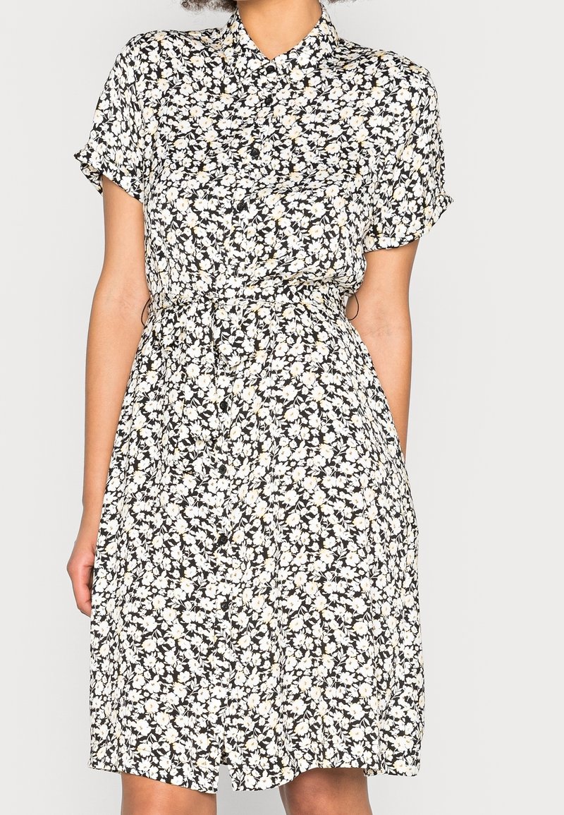 Robe noire à motif floral blanc et jaune, manches courtes, boutonnée sur le devant, taille cintrée, et jupe longueur genou.