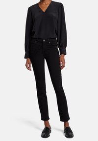 Blusa de satén negra con escote en V y mangas largas gathering, combinada con jeans negros ajustados. El calzado son mocasines negros brillantes.