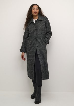 Lange zwart en grijs geblokte jas met een kraag, knoopsluiting, zijzakken en licht oversized mouwen. Gekozen over een wit shirt.