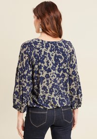 Bloemige blouse met marineblauwe bloemen op een olijfgroene achtergrond, voorzien van lange pofmouwen en een losse fit in de taille.