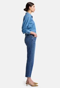 Chemise en denim bleu clair, accompagnée d'un jean droit bleu. Les chaussures présentent un imprimé serpent jaune avec un petit talon. Vue de côté.