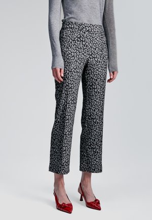 Pantalones de talle a medida con estampado de leopardo en negro y gris, de corte recto; combinados con zapatos de tacón rojos y una blusa gris de manga larga.