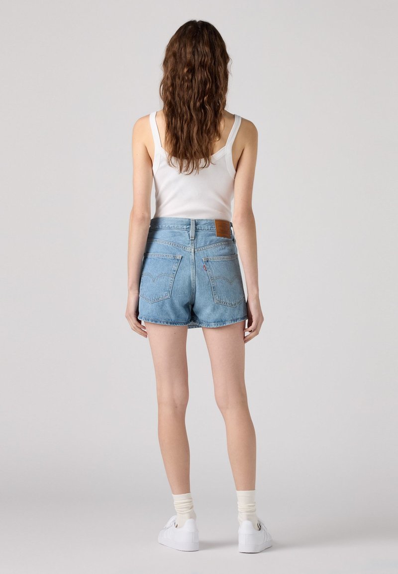 Helle blaue Jeansshorts mit hoher Taille, ausgefranstem Saum und Gesäßtaschen. Mit einem braunen Leder-Label-Patch am Bund.