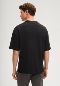 Czarna bawełniana koszulka z krótkim rękawem, prostym krojem i okrągłym dekoltem. Posiada małą czerwoną metkę z logo z boku.