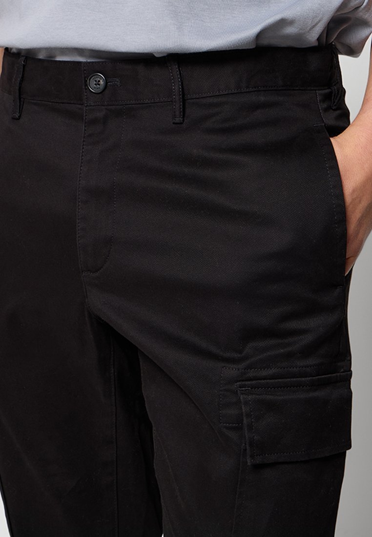 Pantalons cargo noirs en tissu résistant, dotés d'une fermeture à bouton, de poches latérales et d'une finition texturée. Design minimaliste avec des détails fonctionnels.