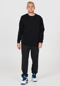 Svart sweatshirt med långa ärmar, rund halsringning och ribbad mudd. Matchad med svarta byxor och vita sneakers med blå detaljer.