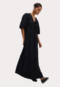 Maxi-Schwarzes Kleid aus strukturiertem Stoff, mit puffärmel und V-Ausschnitt. Mit einer Kordelzug-Detaillierung an der Taille und einer fließenden Silhouette.