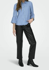 Chemise en denim bleu clair avec boutonnière et manches volantées, associée à un pantalon en cuir noir et des bottines à bout carré.