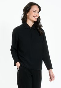 Juodas ilgomis rankovėmis palaidinė su apykakle, turinti priekį užtrauktuku ir lygiu paviršiumi. Derinama su juodomis kelnėmis, sukuriant elegantišką įvaizdį.