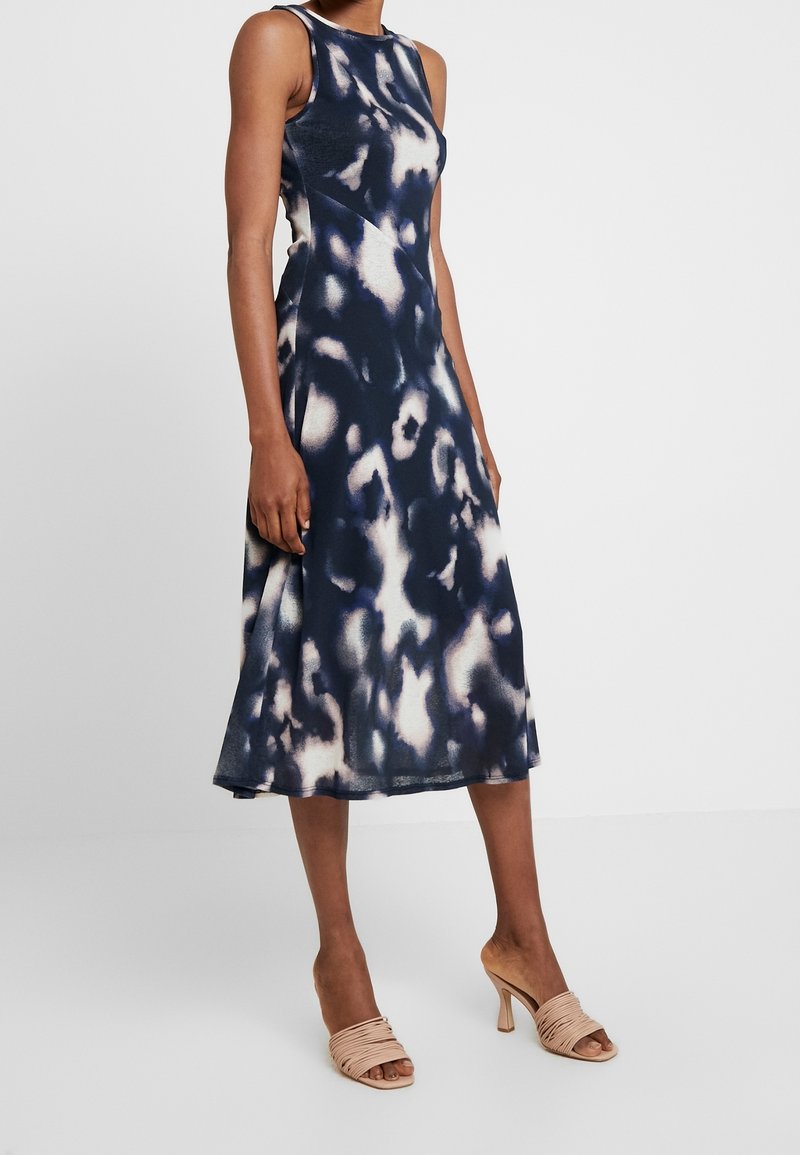 Abito midi tie-dye blu navy e crema con corpetto aderente, design senza maniche e orlo svasato. Abbinato a sandali con tacco a fascia beige.