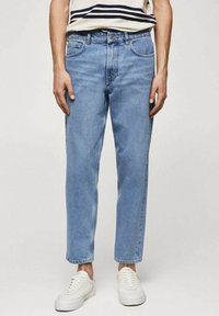 Jeans in denim azzurro chiaro con taglio dritto, cinque tasche e una finitura leggermente sbiadita. Indossati con sneakers bianche.