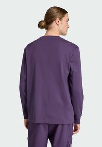 Long-sleeve purple pullover made from soft fabric, featuring a classic crew neckline and relaxed fit, with minimal stitching details.