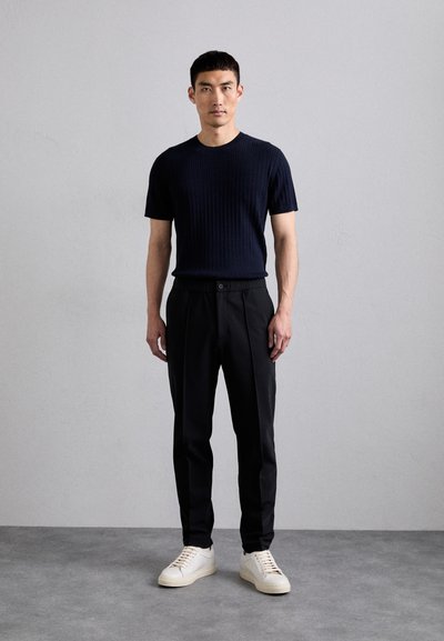Navy-blaues, geripptes T-Shirt mit kurzen Ärmeln, kombiniert mit schwarzen, taillierten Hosen und weißen Sneakers. Einfaches und sauberes Design mit minimalen Akzenten.